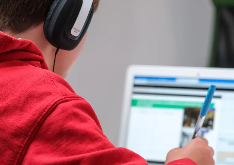 un enfant de dos en face d'un ordinateur portable avec un casque audio sur les oreilles